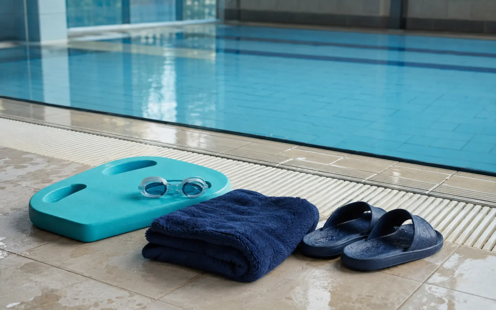 Schwimmbrille, Schwimmbrett, Handtuch und Badesandalen am Beckenrand vor der ersten Schwimmstunde eines Kindes